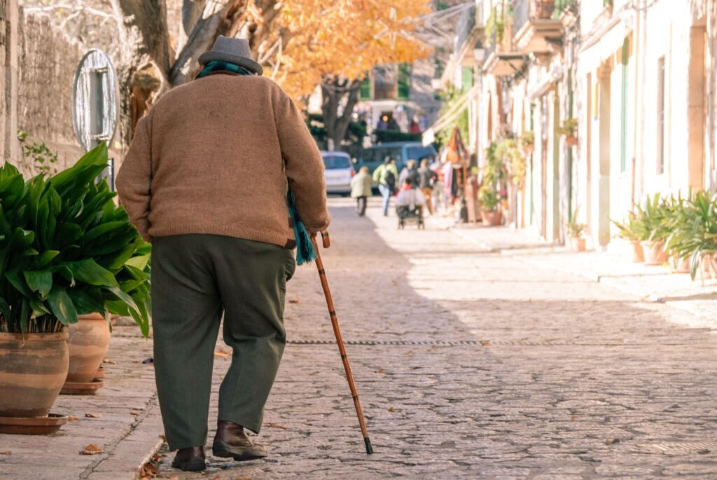 An elderly man with a cane walks along a charming street in Valldemosa, Spain.